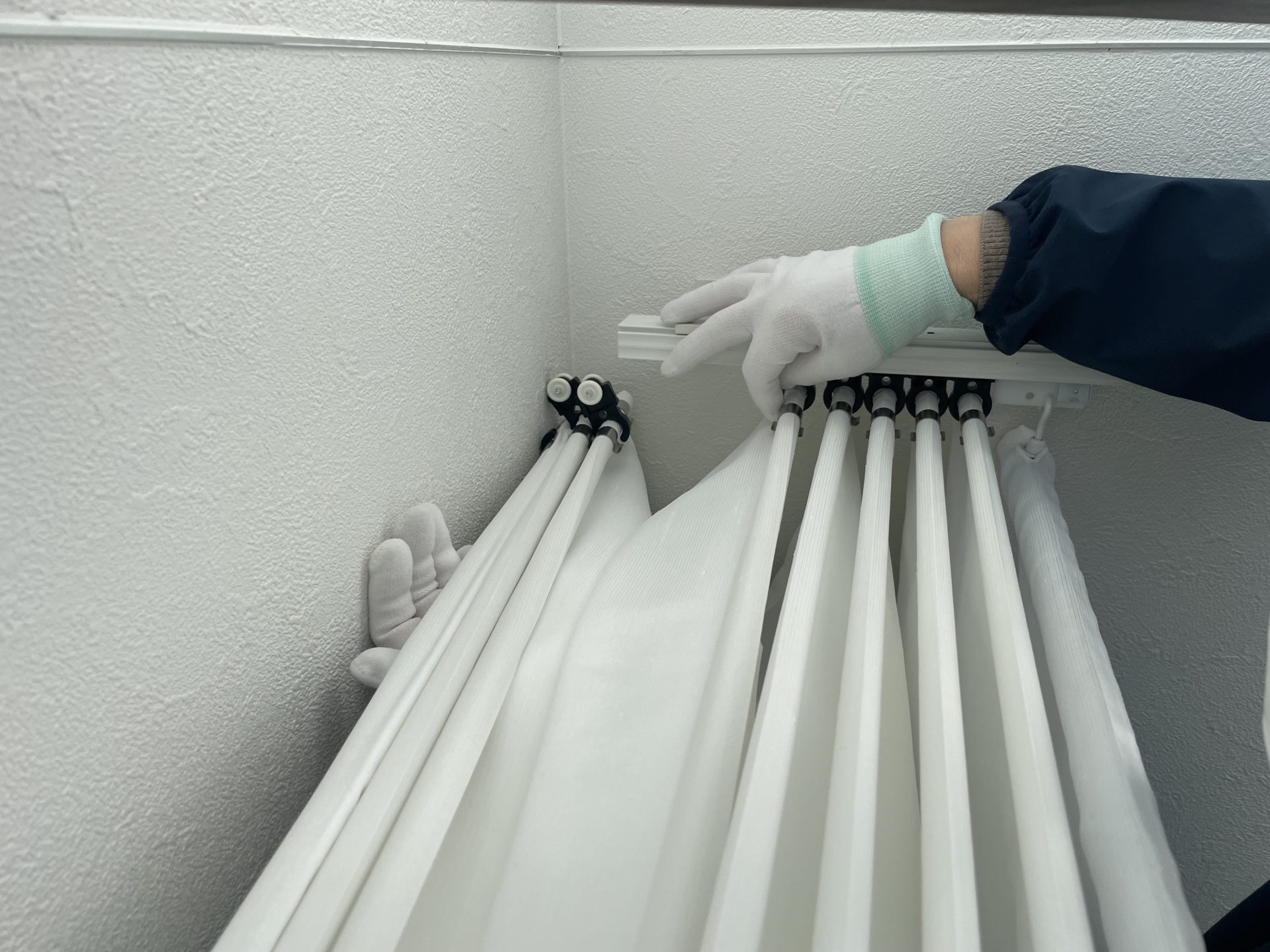 天幕カーテンのランナーをレールの溝に挿入する様子。壁ギリギリの緻密な作業工程