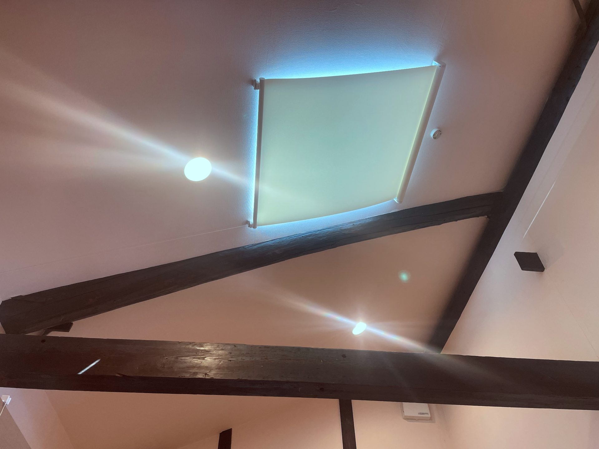 ダイニングの傾斜高窓に取り付けられた白い遮熱ロールスクリーン。傾斜角度30度でもたわみなくフィットしている様子